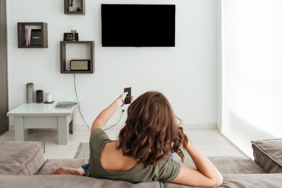 Ver papel pintado de una mujer modelo sentada en un sofá y viendo la televisión en casa